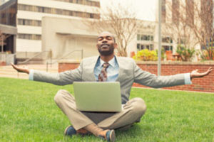 Young businessman with computer relaxing outside corporate office sitting on green grass in mediation mode