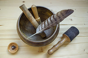 Tibetan singing bowl with mallets and hawk feather on a wooden background. Ringing asian bowl made of metal.